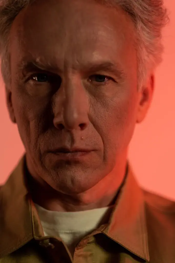 Dramatic close-up of a senior man with intense expression against a warm backdrop.