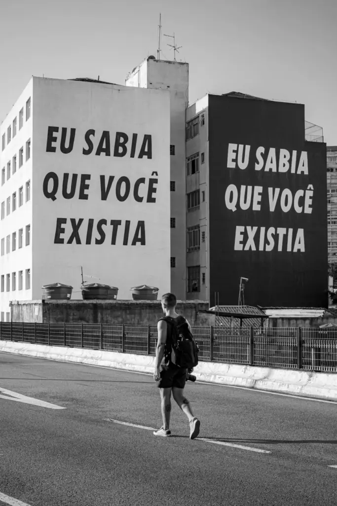Black and white photo of a city street with bold text on buildings and a pedestrian.