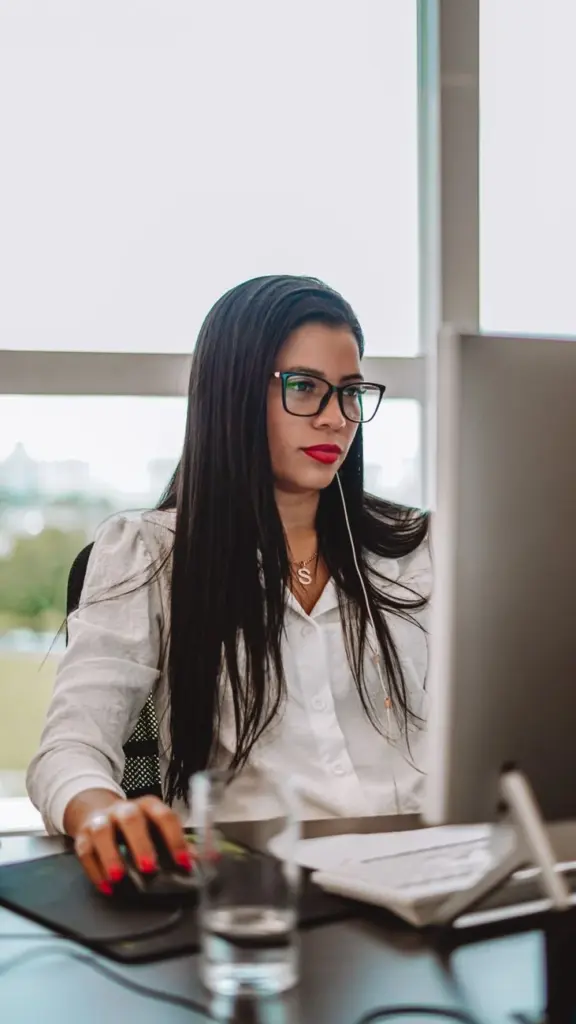 Focused woman with glasses working at a desk in an office environment.