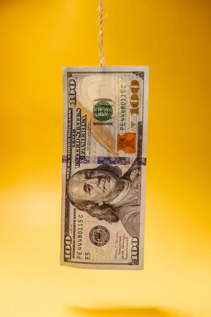 One hundred dollar bill hanging against a bright yellow backdrop, showcasing currency prominently.