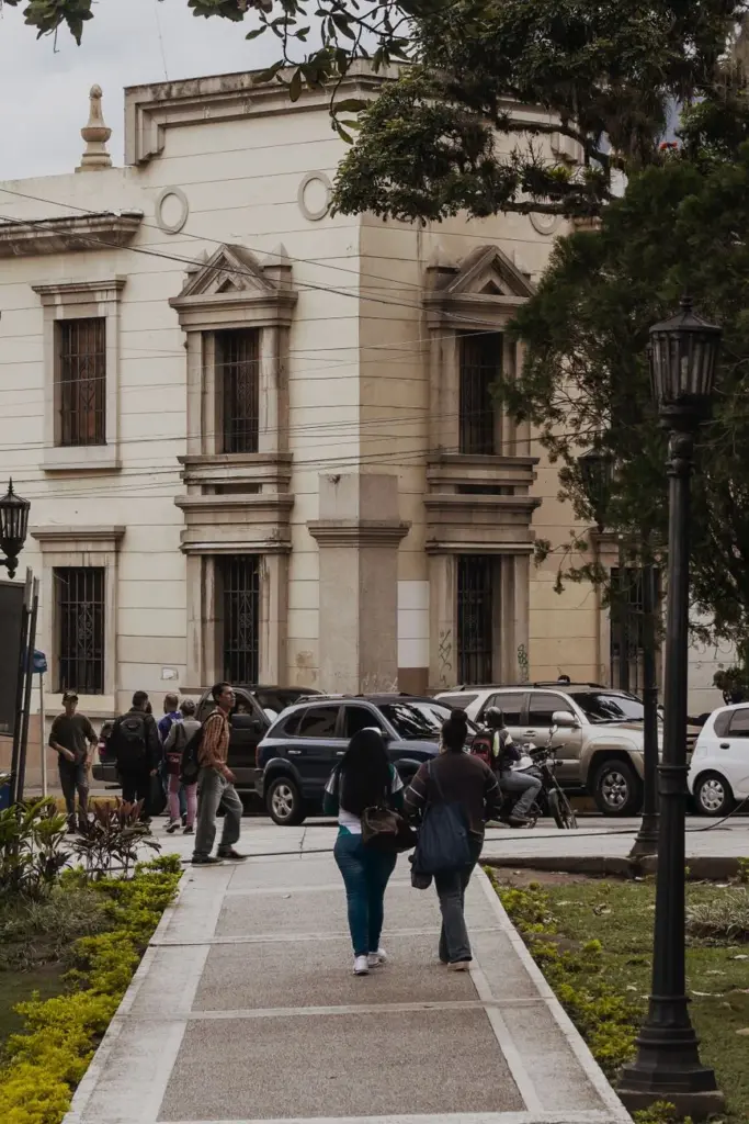 People walking on a street in Mérida, Venezuela, featuring historic architecture and parked cars.