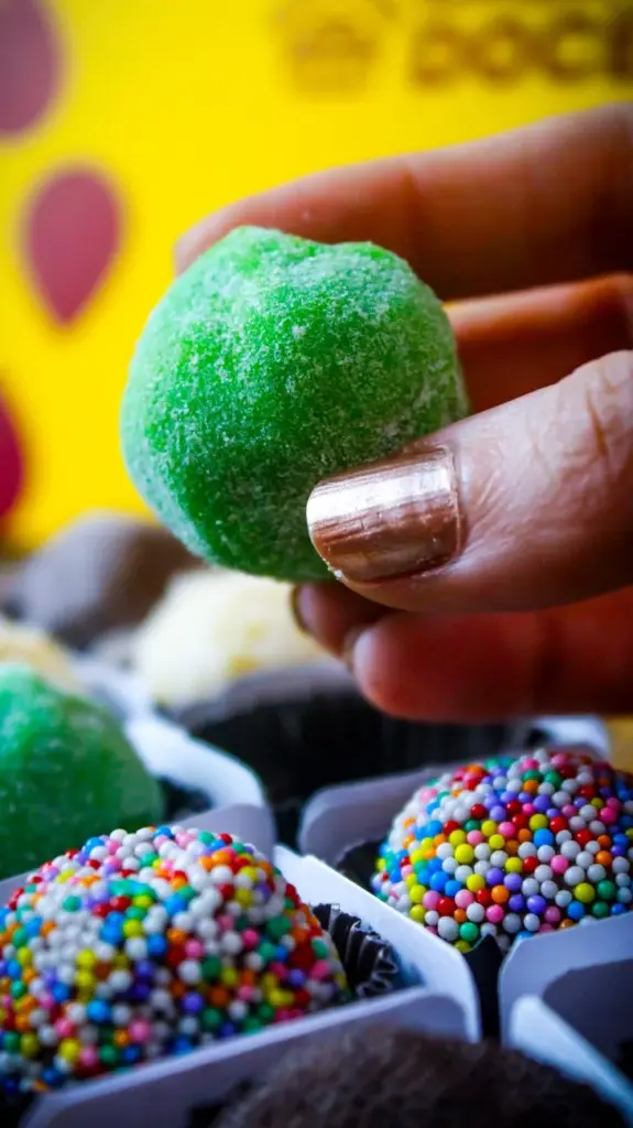 Close-up of assorted Brazilian brigadeiros, including a green sugar-coated sweet, in vibrant colors.