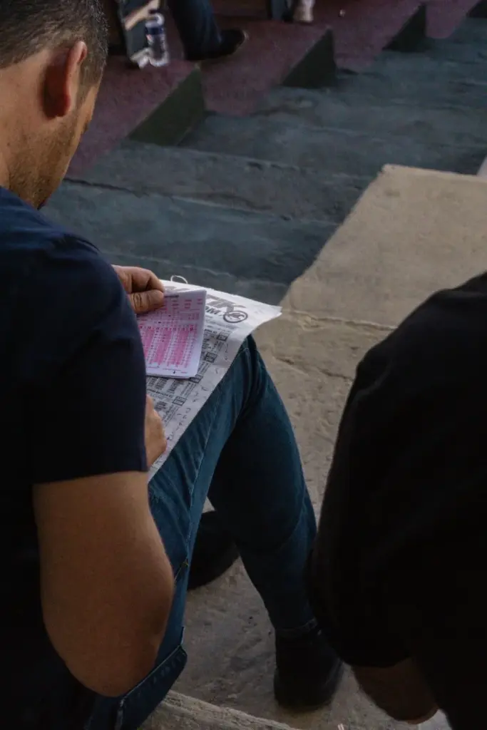 Man sitting on steps analyzing a racing form, focusing on betting strategies.