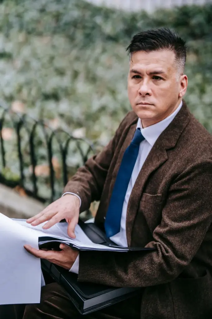 A pensive businessman in formal attire reviewing documents in an outdoor setting.