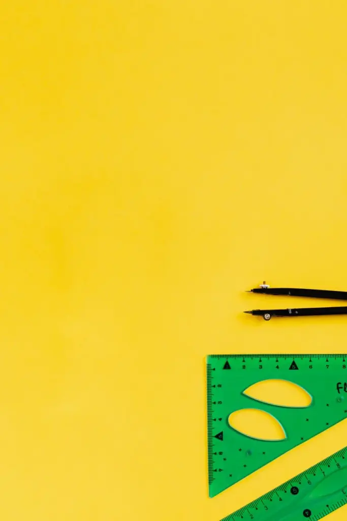 Compass and ruler set on vibrant yellow background with ample copy space.