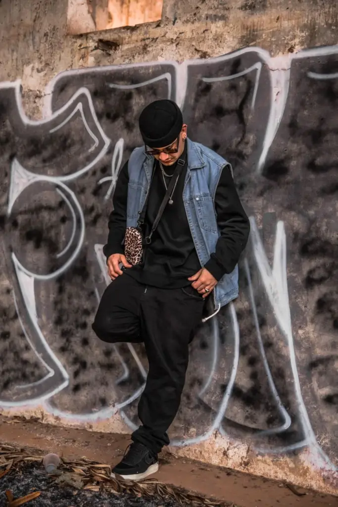 Stylish young man in urban streetwear poses against a graffiti wall.